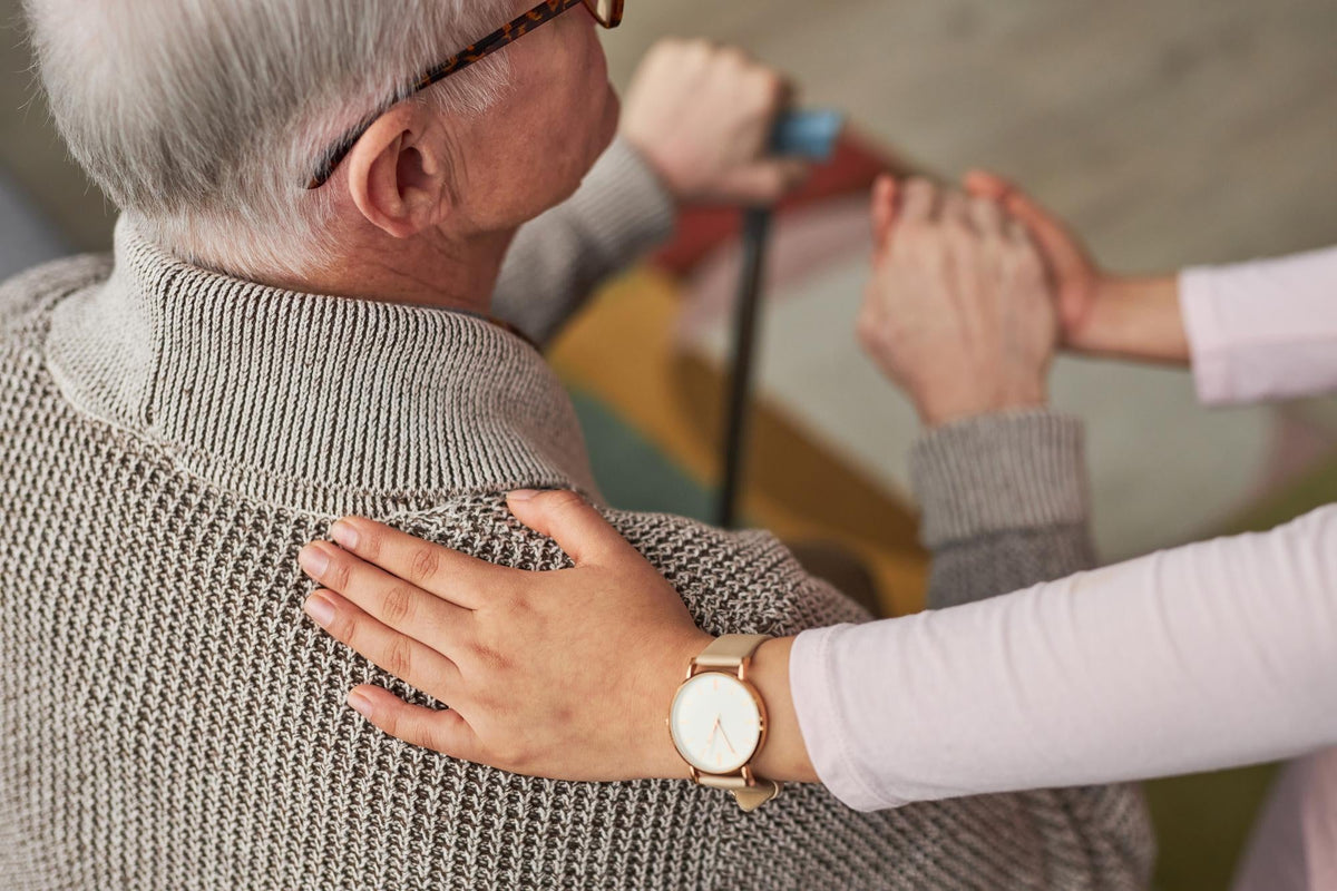 Femme qui met sa main dans le dos d'un homme âgé assis 