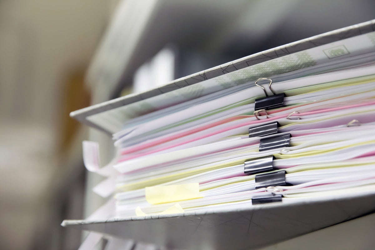 Pile de dossiers administratifs maintenus par des pinces, illustrant la constitution d'un dossier de demande d'AAH auprès de la MDPH