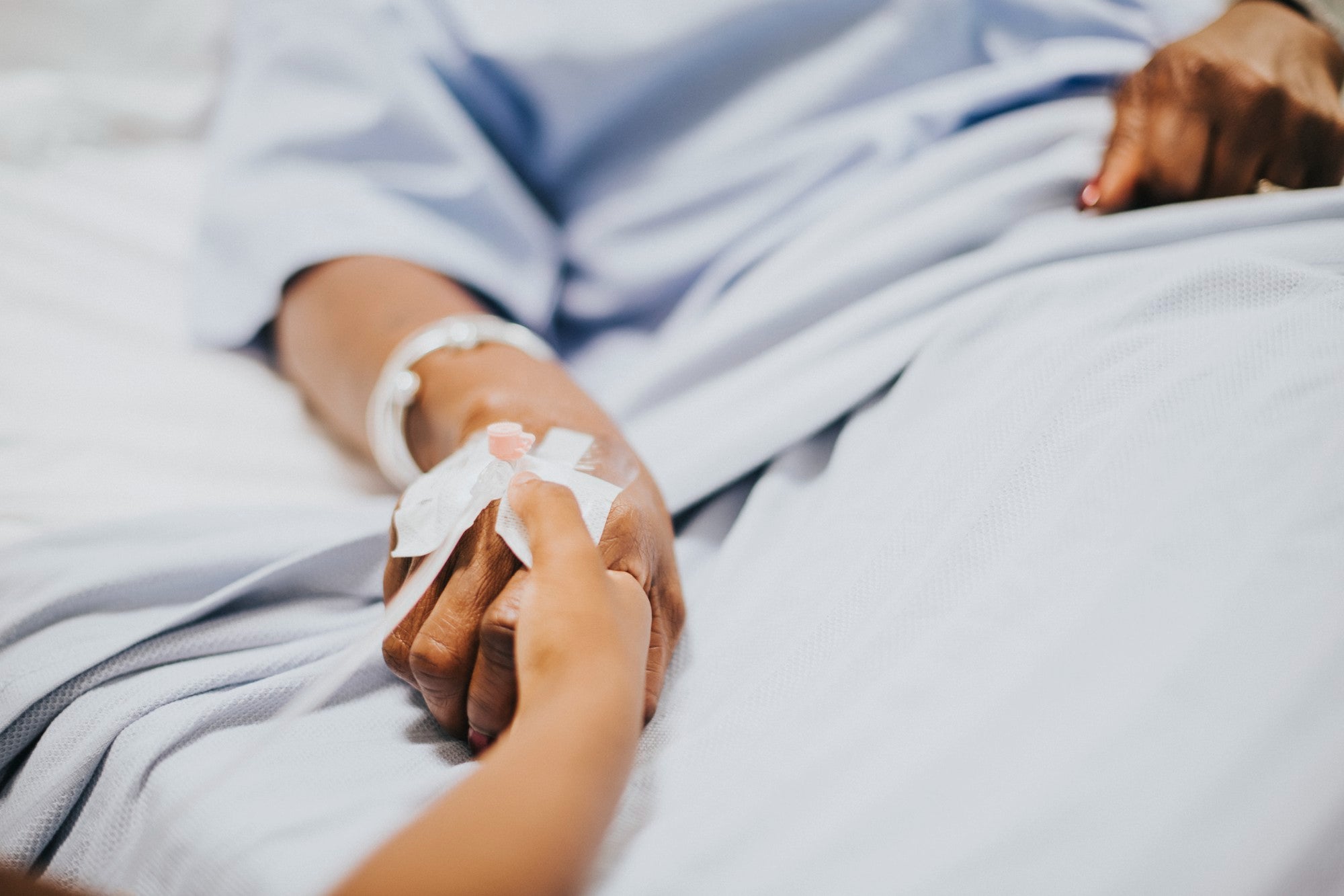 main qui tient la main d'une autre personne dans un lit medicalisé 